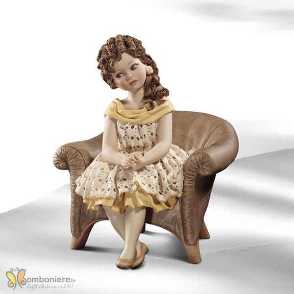Bambola di porcellana seduta su una poltrona marrone con abito in pizzo bianco e giallo